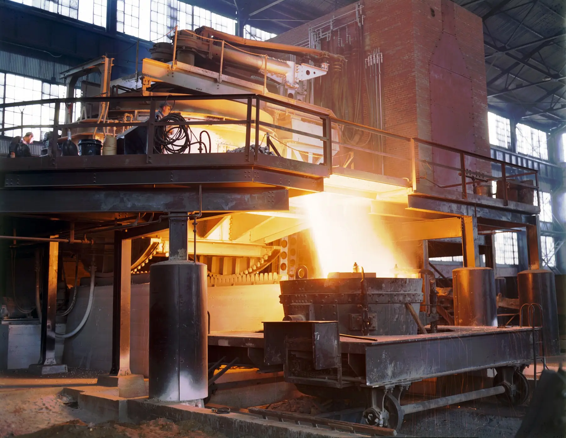 Molten steel pouring from an electric furnace into a ladle, the whole mill lit orange